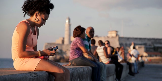 In this March 11, 2014 photo, a woman uses her cellphone as she sits on the Malecon in Havana, Cuba. The U.S. Agency for International Development masterminded the creation of a "Cuban Twitter," a communications network designed to undermine the communist government in Cuba, built with secret shell companies and financed through foreign banks, The Associated Press has learned. The project, which lasted more than two years and drew tens of thousands of subscribers, sought to evade Cubas stranglehold on the Internet with a primitive social media platform. (AP Photo/Franklin Reyes)