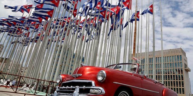 FILE - In this July 26, 2015, file photo, a classic American convertible car passes beside the United States embassy as Cuban flags fly beside in Havana, Cuba. The U.S. doesnt plan to invite Cuban dissidents to Secretary of State John Kerrys historic flag-raising at the American Embassy in Havana on Aug. 14, illustrating a shift in U.S. policy from the islands opposition to its government. (AP Photo/Desmond Boylan, File)