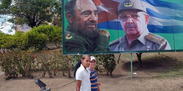 SANTIAGO DE CUBA, CUBA - MARCH 27: Two teens walk by a billboard of Fidel and Raul Castro a day after Pope Benedict XVI held a historic mass in the city on March 27, 2012 in Santiago de Cuba. Fourteen years after Pope John Paul II visited Cuba, Pope Benedict is making his first trip to the communist country. Benedict, who arrived from Mexico, conducted a mass in the city of Santiago de Cuba first followed by a mass in Havana before leaving on the 28th. Tensions are high in Cuba between dissidents and the government as activists hope the international exposure of the Papal visit will result in renewed attention to their struggle for greater freedoms. (Photo by Spencer Platt/Getty Images)