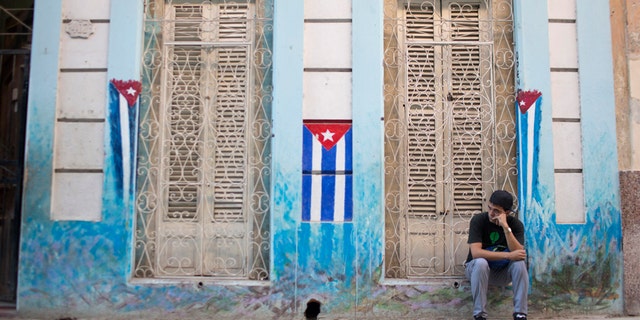 File photo - A man sits on the sidewalk next to Cuban National flags painted on the walls in downtown Havana, Jan. 22, 2015.