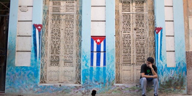 File photo - A man sits on the sidewalk next to Cuban National flags painted on the walls in downtown Havana, Jan. 22, 2015.