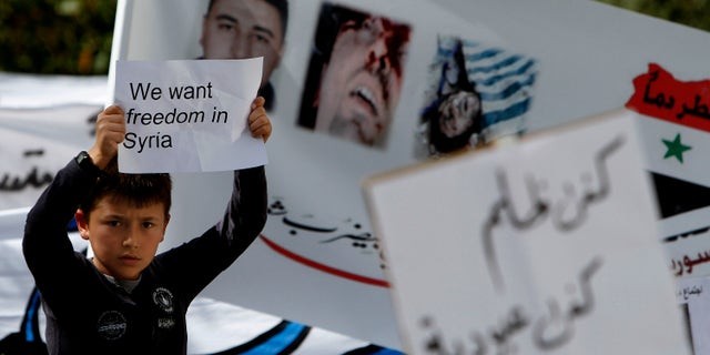 A Syrian boy resident in Cyprus holds a banner during a protest against the Syrian president Bashar Al-Assad outside the Syrian embassy, Friday, April 1, 2011.