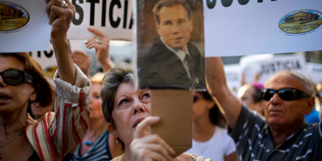 A woman chants the Argentine national anthem holding a portrait of the late prosecutor Alberto Nisman outside the AMIA Jewish community center in Buenos Aires, Argentina, Wednesday, Jan. 21, 2015. Nisman, who had been investigating the 1994 bombing of the Jewish community center that killed 85 people and who accused President Cristina Fernandez of shielding Iranian suspects, was found dead from a gunshot to the head, in his apartment late Sunday, hours before he was to testify in a Congressional hearing about the case. (AP Photo/Rodrigo Abd)