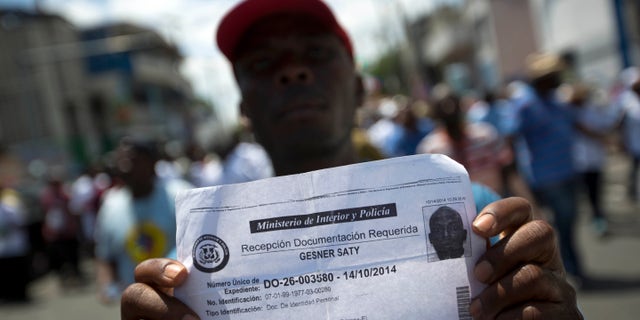 FILE - In this July 21, 2015, file photo, deported Haitian man holds up his document that confirms he turned in paperwork to apply for legal residency in the Dominican Republic during a march to the prime minister's office to protest the DR's deportation of Haitians in Port-au-Prince, Haiti. The sharply uneven situation for non-citizens stems from a 2013 ruling by the Dominican Constitutional Court in a decades-long dispute over who is entitled to citizenship. (AP Photo/Dieu Nalio Chery, File)