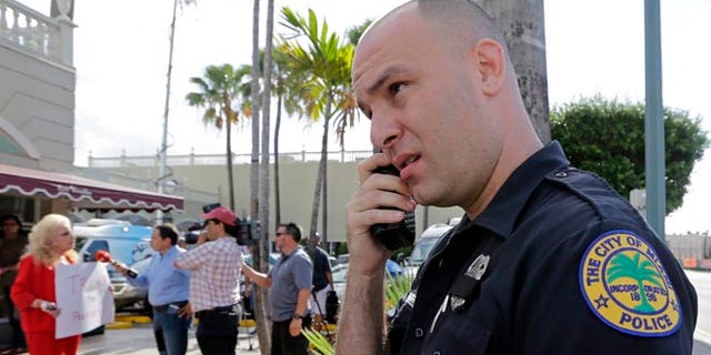 City of Miami police officer R. Delgado covers his badge with a black band as he honors the death of police officers in Dallas, Friday, July 8, 2016, at a Republican presidential candidate Donald Trump campaign stop. Trump has called off his two Friday campaign events in Miami in the wake of deadly sniper killings of Dallas police officers. (AP Photo/Alan Diaz)