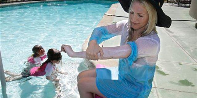 In this Wednesday, June, 22, 2011, photo, a woman who was diagnosed with malignant melanoma at 35 puts on sun screen while poolside with her daughters at their home in Carmichael, Calif.