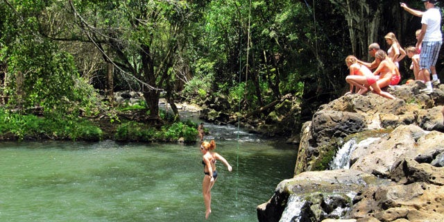 In a photo made July 6, 2011, a woman jumps into Kipu Falls in Lihue, Hawaii, on the island of Kauai.  But the alluring beauty of the waterfall and natural pool conceals a deadly side. Five visitors to Kauai, all male, have drowned at Kipu Falls in the past five years. (AP Photo/Audrey McAvoy)