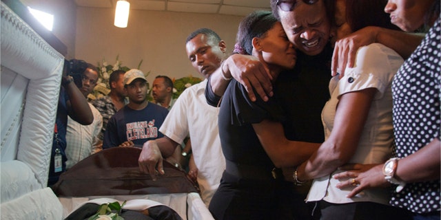 Kansas City Royals player Edinson Volquez, third from Right, embraces his sister Wendy Volquez, left, and mother Ana Ramirez as they stand next to the body of his father during his wake at a funeral home in Santo Domingo, Dominican Republic, Wednesday, Oct. 28, 2015. (AP Photo/Tatiana Fernandez)