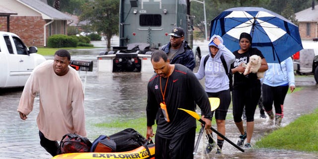 Residents use a raft to evacuate as others walk out of their neighbor Saturday, Aug. 13, 2016, in Baton Rouge, La.