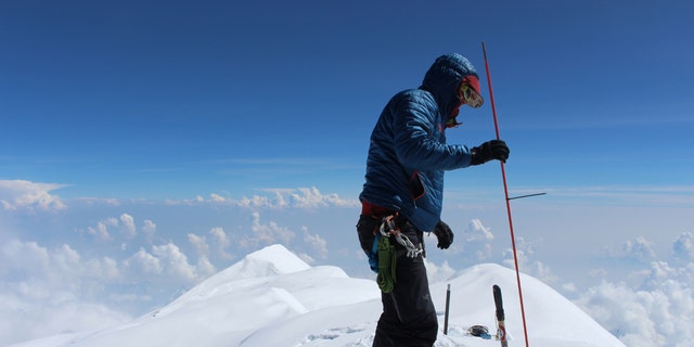 In this June 24, 2015, photo provided by Compass Data/USGS, Blaine Horner of CompassData probes the snow pack at the highest point in North America along with setting up Global Position System equipment for precise summit elevation data on top of Denali in Denali National Park, Ak.