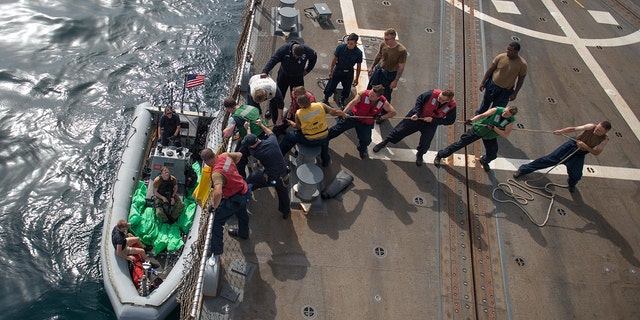 U.S. Navy Sailors aboard the guided-missile destroyer USS Jason Dunham heave a line to load the seized weapons.