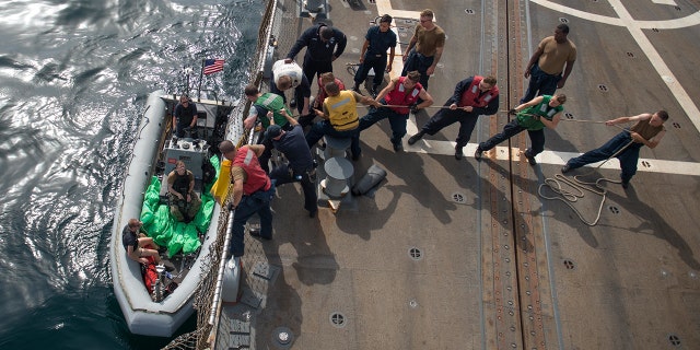 U.S. Navy Sailors aboard the guided-missile destroyer USS Jason Dunham heave a line to load the seized weapons.