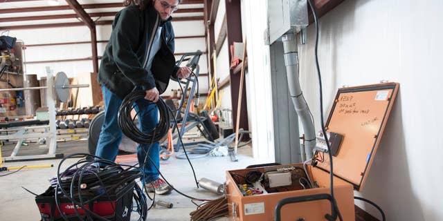 This handout photo, taken Jan. 16, 2014, provided by Southern Methodist University, shows Remi Oldham, an SMU geophysics graduate student, running a cable to connect the seismometer to communications interface equipment housed in the orange metal box in Willow Park, Texas. The interface equipment allows the transmission of the data collected by the seismometer back to SMU. With real-time monitors, scientists linked a swarm of small earthquakes west of Fort Worth, Texas, to nearby natural gas wells and wastewater injection. In 84 days from November 2013 to January 2014, the area around Azle, Texas, shook with 27 magnitude 2 or greater earthquakes, while scientists at Southern Methodist University and the U.S. Geological Survey monitored the shaking. It’s an area that had no recorded quakes for 150 years on faults that “have been inactive for hundreds of millions of years,” said SMU geophysicist Matthew Hornbach. (Hillsman Stuart Jackson/SMU via AP) SMU, Dedman School of Humanities, Geology, Research, Seismic, Off Campus, Willow Park, Texas, Secondary Fire Station, Heather Deshon, Chris Hayward, Remi Oldham