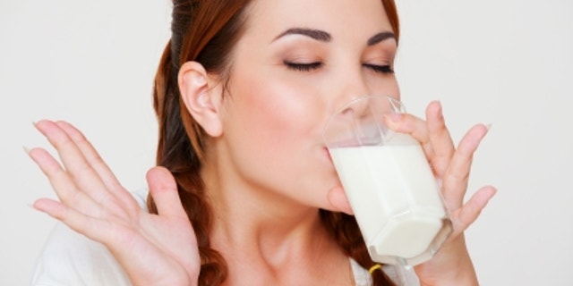 happy young woman drinking milk over grey background