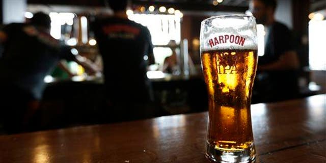 In this July 1, 2013 photo a glass of Rich and Dan's Rye IPA rests on the counter as bartenders pour drafts for patrons in the Beer Hall at the Harpoon Brewery in the Seaport District of Boston.