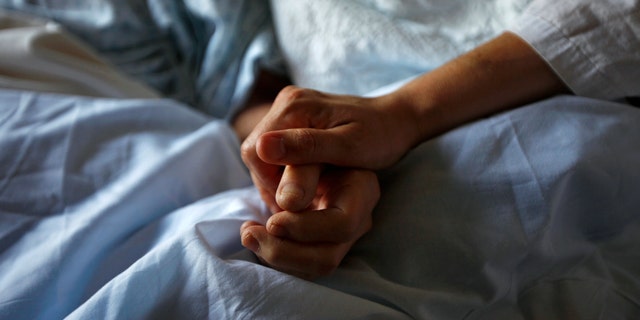 A woman holds the hand of her mother who is dying from cancer during her final hours at a palliative care hospital.