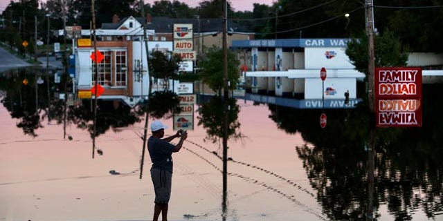 Oct. 7, 2015: Gay Miller takes photos of E. Main Street in downtown Kingstree, S.C., as the Black River floodwaters reflect in the late afternoon light. (AP Photo/Mic Smith)