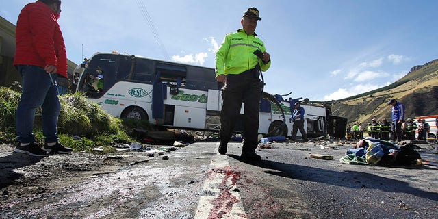 A police officer walks past a Colombian-registered bus traveling to Quito that crashed in Pifo, Ecuador, Tuesday, Aug. 14, 2018. At least 24 people were killed and another 19 injured when a bus careened into another vehicle at high speed and overturned along the Pifo-Papallacta highway, near Ecuador's capital, local officials reported.