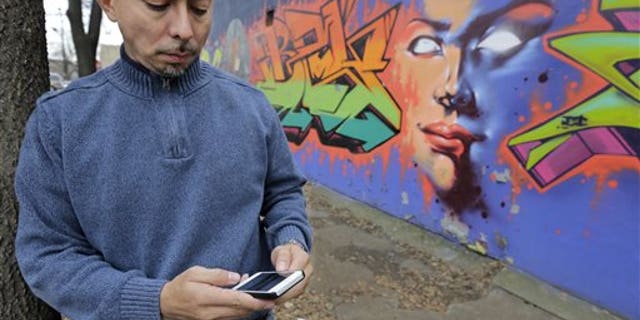 In this Dec. 6, 2013 photo, Eddie Bocanegra, co-executive director of the YMCA of Metropolitan Chicago's Youth Safety and Violence Prevention program, stands with his phone outside the organization's center in the Pilson neighborhood of Chicago. With the advent of social media usage by gangs, he says, "In the past you would have gangs approach you and say, 'Listen we're from the 'hood. Maybe you should get involved.' Now the kids are going to the gangs saying, 'I saw this. How can I be a part of it?'" (AP Photo/M. Spencer Green)