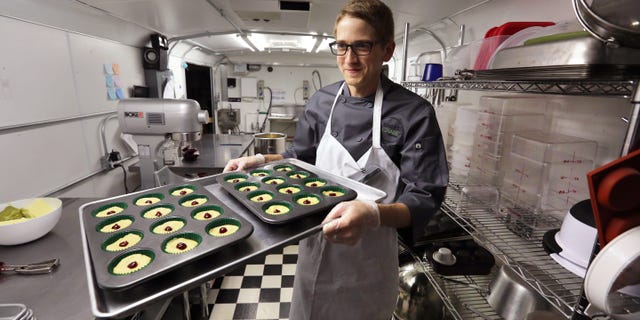 FILE - In this June 19, 2014, file photo, chef Alex Tretter carries a tray of cannabis-infused peanut butter and jelly cups to the oven for baking at Sweet Grass Kitchen, a well-established Denver-based gourmet marijuana edibles bakery which sells its confections to retail outlets throughout the state. Colorado marijuana regulators have drafted an emergency rule aimed at making it easier for new marijuana users to tell how much pot they are eating. (AP Photo/Brennan Linsley, File)