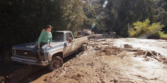 FILE - In this Feb. 24, 1998 file photo, a woman waits for a tow truck on the hood of her brother's pickup after a wall of mud plowed down Laguna Beach Canyon Road in Orange County, Calif. forcing her to evacuate her home, in background. A long anticipated El Nino weather warping is finally here. But for drought-struck California, it’s too little, too late, meteorologists say. The National Weather Service Thursday proclaimed the somewhat infamous weather phenomenon El Nino is now in place. It’s a warming of a certain patch of the central Pacific that changes weather patterns worldwide, associated with flooding in some places, droughts elsewhere, a generally warmer globe, and fewer Atlantic hurricanes. El Ninos are usually so important that economists even track it because of how it affects commodities. This year's El Nino that has arrived isn’t big and is late so it’s unlikely to do much to alleviate the current California drought. (AP Photo/Nick Ut, File)