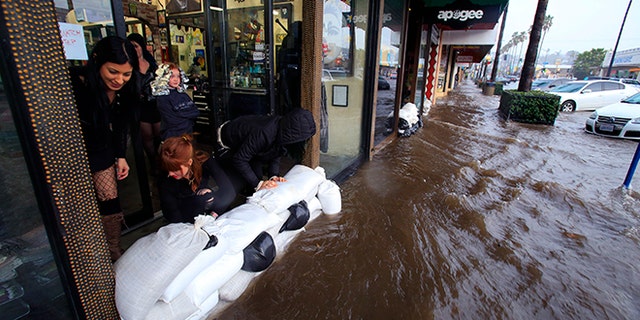 From left, Amanda Bourbois, Mary Spear and Jordan Brown place sand bags in front of the Electric Chair salon Wednesday, Jan. 6, 2016, in San Diego. El Nino storms lined up in the Pacific, promising to drench parts of the West for more than two weeks and increasing fears of mudslides and flash floods in regions stripped bare by wildfires. (Nelvin C. Cepeda/The San Diego Union-Tribune via AP)  NO SALES; MANDATORY CREDIT