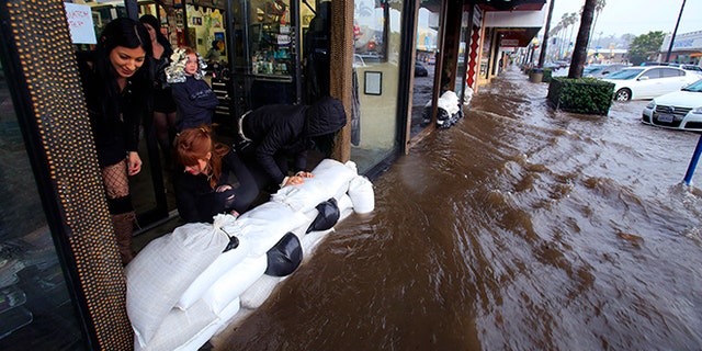 From left, Amanda Bourbois, Mary Spear and Jordan Brown place sand bags in front of the Electric Chair salon Wednesday, Jan. 6, 2016, in San Diego. El Nino storms lined up in the Pacific, promising to drench parts of the West for more than two weeks and increasing fears of mudslides and flash floods in regions stripped bare by wildfires. (Nelvin C. Cepeda/The San Diego Union-Tribune via AP) NO SALES; MANDATORY CREDIT