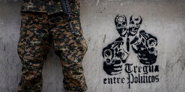 In this June 14, 2016 photo, a soldier stands next to a stenciled graffiti that reads in Spanish "Truce between politicians" painted on the main walls of the National Palace in San Salvador, El Salvador. After becoming the world's murder capital last year and posting an equally bloody start to 2016, El Salvador has seen its monthly homicide rates fall by about half. The government attributes the drop to a tough military crackdown on the country's powerful gangs, while the gangs themselves claim credit for a nonaggression pact between the three biggest criminal groups. (AP Photo/Salvador Melendez)