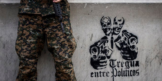 In this June 14, 2016 photo, a soldier stands next to a stenciled graffiti that reads in Spanish "Truce between politicians" painted on the main walls of the National Palace in San Salvador, El Salvador. After becoming the world's murder capital last year and posting an equally bloody start to 2016, El Salvador has seen its monthly homicide rates fall by about half. The government attributes the drop to a tough military crackdown on the country's powerful gangs, while the gangs themselves claim credit for a nonaggression pact between the three biggest criminal groups. (AP Photo/Salvador Melendez)