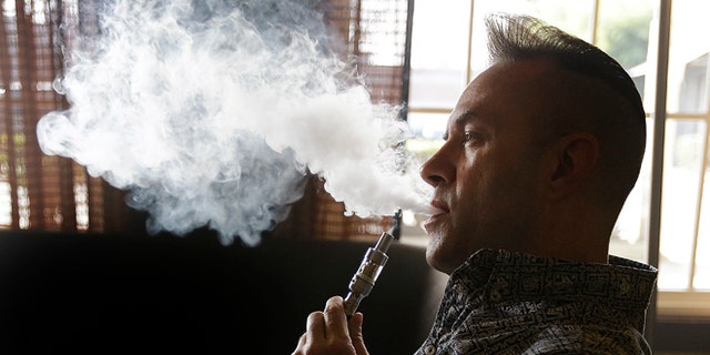 Geoff Braithwaite, owner of Tasty Vapor, exhales vapor after using an electronic cigarette Wednesday, Jan. 28, 2015, in Oakland, Calif. California health officials on Wednesday declared electronic cigarettes a health threat that should be strictly regulated like tobacco products, joining other states and health advocates across the U.S. in seeking tighter controls as "vaping" grows in popularity. The California Department of Public Health report says e-cigarettes emit cancer-causing chemicals and get users hooked on nicotine but acknowledges that more research needs to be done to determine the immediate and long-term health effects. (AP Photo/Ben Margot)