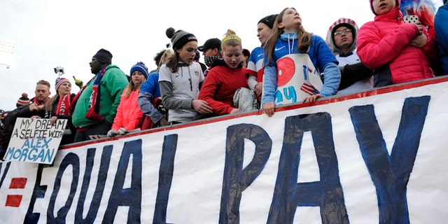 Fans stand behind a large sign for equal pay for the women's soccer team during an international friendly soccer match between the United States and Colombia at Pratt &amp; Whitney Stadium at Rentschler Field, Wednesday, April 6, 2016, in East Hartford, Conn. (AP Photo/Jessica Hill)