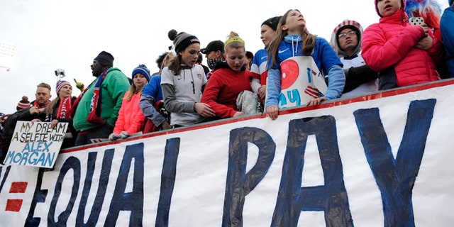 Fans stand behind a large sign for equal pay for the women's soccer team during an international friendly soccer match between the United States and Colombia at Pratt & Whitney Stadium at Rentschler Field, Wednesday, April 6, 2016, in East Hartford, Conn. (AP Photo/Jessica Hill)