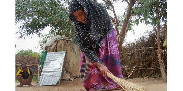 April 27, 2014: Ubah Mohammed Abdule, 33, center, sweeps the floor outside her hut as her son Abdullahi Yusuf Ahmed, 8, left, looks on in the Shedder refugee camp near the town of Jigjiga, in far eastern Ethiopia. (AP Photo/Elias Asmare)