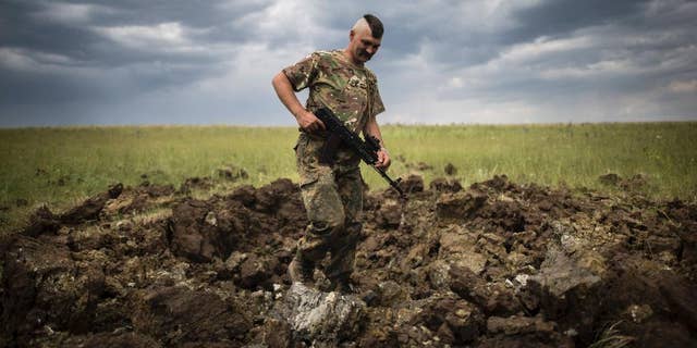 FILE - In this Monday, June 15, 2015 file photo, a Ukrainian serviceman investigates a crater left by a Grad rocket in the village of Toshkivka, Luhansk region, eastern Ukraine. (AP Photo/Evgeniy Maloletka, File)
