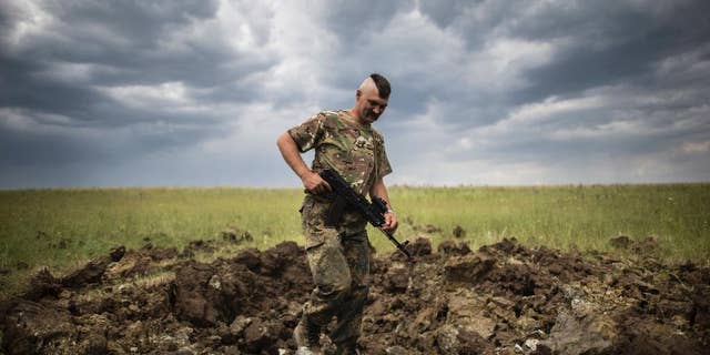 FILE - In this Monday, June 15, 2015 file photo, a Ukrainian serviceman investigates a crater left by a Grad rocket in the village of Toshkivka, Luhansk region, eastern Ukraine. (AP Photo/Evgeniy Maloletka, File)