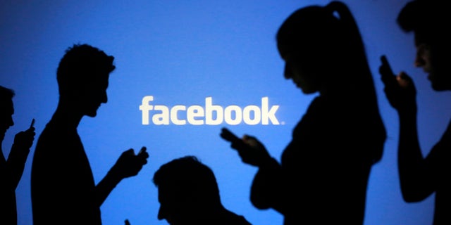 People are silhouetted as they pose with mobile devices in front of a screen projected with a Facebook logo, in this picture illustration taken in Zenica October 29, 2014. Facebook Inc warned on Tuesday of a dramatic increase in spending in 2015 and projected a slowdown in revenue growth this quarter, slicing a tenth off its market value. Facebook shares fell 7.7 percent in premarket trading the day after the social network announced an increase in spending in 2015 and projected a slowdown in revenue growth this quarter. REUTERS/Dado Ruvic (BOSNIA AND HERZEGOVINA - Tags: BUSINESS SCIENCE TECHNOLOGY BUSINESS LOGO) - RTR4C0UZ