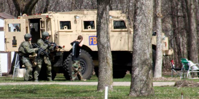 FILE - This May 3, 2013, photo provided by Jeremy Jones shows authorities with Buford Rogers, right, who belongs to a tiny local militia, during a raid on a mobile home in Montevideo, Minn. Rogers, 25, is scheduled to be sentenced Monday, April 28, 2011 after pleading guilty to one count of possessing a firearm illegally and one count of possessing an unregistered destructive device, namely "two black powder and nail devices," which he admitted he made himself. Prosecutors are seeking more than five years in prison, arguing that Rogers poses a threat to public safety, noting the items were designed solely to injure people. (AP Photo/Montevideo American-News, Jeremy Jones, File) MANDATORY CREDIT