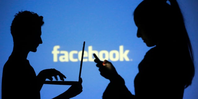 People are silhouetted as they pose with laptops in front of a screen projected with a Facebook logo, in this picture illustration taken in Zenica October 29, 2014. Facebook Inc warned on Tuesday of a dramatic increase in spending in 2015 and projected a slowdown in revenue growth this quarter, slicing a tenth off its market value. Facebook shares fell 7.7 percent in premarket trading the day after the social network announced an increase in spending in 2015 and projected a slowdown in revenue growth this quarter. REUTERS/Dado Ruvic (BOSNIA AND HERZEGOVINA - Tags: BUSINESS SCIENCE TECHNOLOGY BUSINESS LOGO) - RTR4C0V2