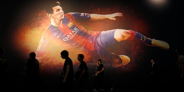 Visitors walk past a placard of "FIFA 15" video game featuring soccer player Lionel Messi at the Gamescom 2014 fair in Cologne Aug. 13, 2014.