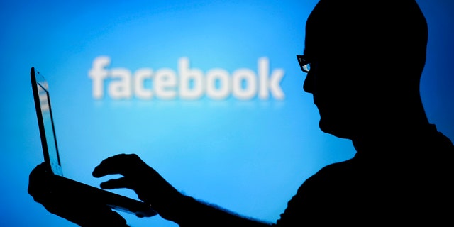 A man is silhouetted against a video screen with an Facebook logo as he poses with an Dell laptop in this photo illustration taken in the central Bosnian town of Zenica, August 14, 2013. REUTERS/Dado Ruvic (BOSNIA AND HERZEGOVINA - Tags: BUSINESS TELECOMS) - RTX12L6I