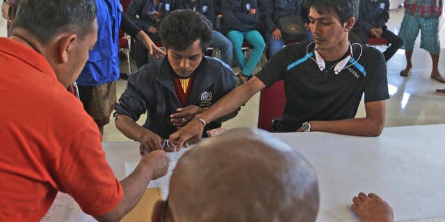 In this Tuesday, Sept. 8, 2015 photo, Burmese fisherman Kyaw Zayar, right, helps his friend Nge Nge, center, to translate a document Nge Nge has to sign in order to receive his unpaid salary in Ambon, Maluku province, Indonesia. Kyaw Zayar is among more than 2,000 fishermen rescued this year from forced labor under brutal conditions, mainly in remote Indonesian islands. The 30-year-old from Myawaddy, Myanmar, was forced to work on a fishing boat for nearly five years. (AP Photo/Achmad Ibrahim)