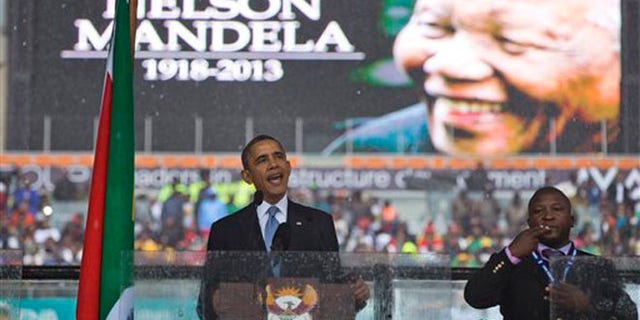 President Barack Obama delivers his speech next to a sign language interpreter during a memorial service at FNB Stadium in honor of Nelson Mandela on Tuesday, Dec. 10, 2013 in Soweto, near Johannesburg.