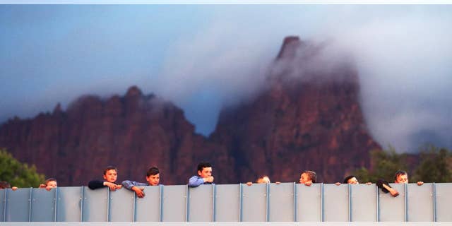 Residents of Hildale, Utah and Colorado City, Ariz., watch as work goes on to clean debris off of a bridge area after a flash flood on Tuesday, Sept. 15, 2015 in Colorado City, Ariz. A wall of water swept away vehicles in the Utah-Arizona border town Monday, killing several people. (Scott G Winterton/The Deseret News via AP) SALT LAKE TRIBUNE OUT; MAGS OUT; MANDATORY CREDIT