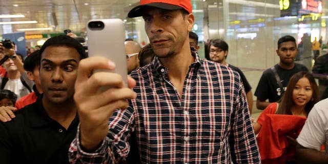 FILE - In this Tuesday, May 13, 2014, Manchester United's Rio Ferdinand takes a "selfie" upon arrival at the Changi International Airport in Singapore. The English Football Association has banned Queens Park Rangers defender Rio Ferdinand for three games over a tweet containing a derogatory reference to women. (AP Photo/Wong Maye-E, File)