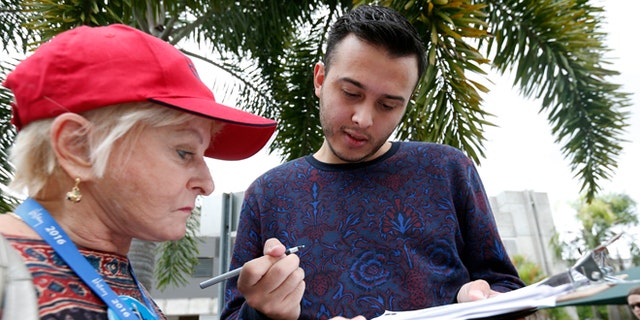 Volunteer Sandi Strickland, left, helps Roman Rodriguez, right, fill out a new voter registration form because of a change of address, as he waits in line to attend a rally for Democratic presidential candidate Hillary Clinton and former vice president Al Gore, Tuesday, Oct. 11, 2016, in Miami. A federal judge has given Democrats a partial victory in the presidential battleground of Florida, extending the state's voter registration deadline one day and agreeing to consider a longer extension in the wake of Hurricane Matthew. (AP Photo/Wilfredo Lee)