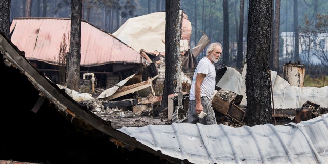 Earl Moss looks over his burned home, foreground, after wildfires swept through his neighborhood on Ridge Road in Eastpoint, Fla., Monday, June 25, 2018. (AP Photo/Mark Wallheiser)