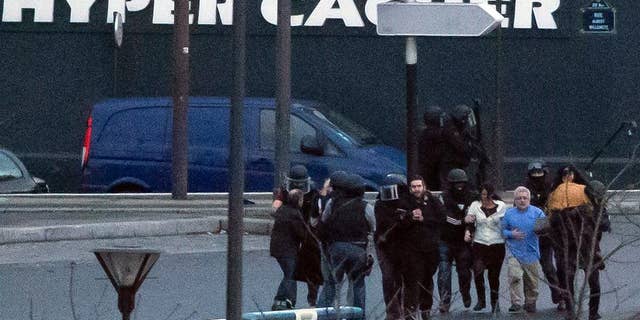 FILE - In this Jan.9, 2015 file photo, security officers escort released hostages after they stormed a kosher market to end a hostage situation, in Paris, France. Families of hostages of a radical gunman who killed four in a kosher supermarket are suing a French broadcaster over its live coverage of the attack, saying it put the hostages’ lives in danger, Paris prosecutor’s office spokeswoman said Friday April 3, 2015. (AP Photo/Michel Euler, File)