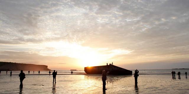People walk on the beach where remnants of the artificial port of Arromanches, still stand in western France, Thursday June 5, 2014. World leaders and veterans prepare to mark the 70th anniversary of the invasion this week in Normandy. (AP Photo/Thibault Camus)