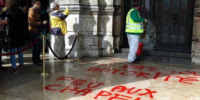 A worker cleans the graffiti at entrance of the Sacre Coeur basilica in the Montmartre district of Paris, Wednesday, March 19, 2014. There were no immediate claims of responsibility for graffiti found at the iconic basilica. Graffiti on the floor reads: Down with any authority. (AP Photo/Thibault Camus)