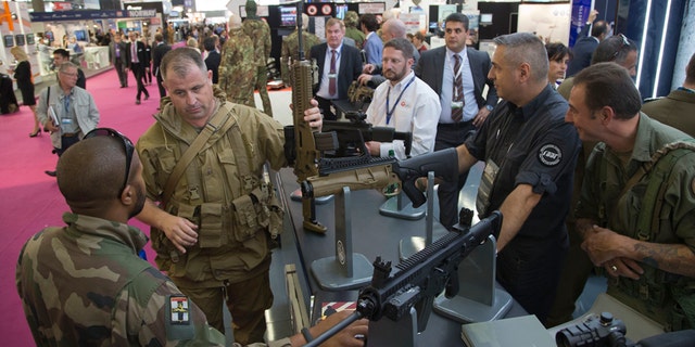 A member of the French army, left, looks at a assault rifle manufactured by US company Beretta, presented at the Eurosatory Defence and Security trade show, in Villepinte, outside Paris, Monday, June 16, 2014. Over 1500 exhibitors will take part in the trade show which takes place in the north of Paris from June 16 to June 20.